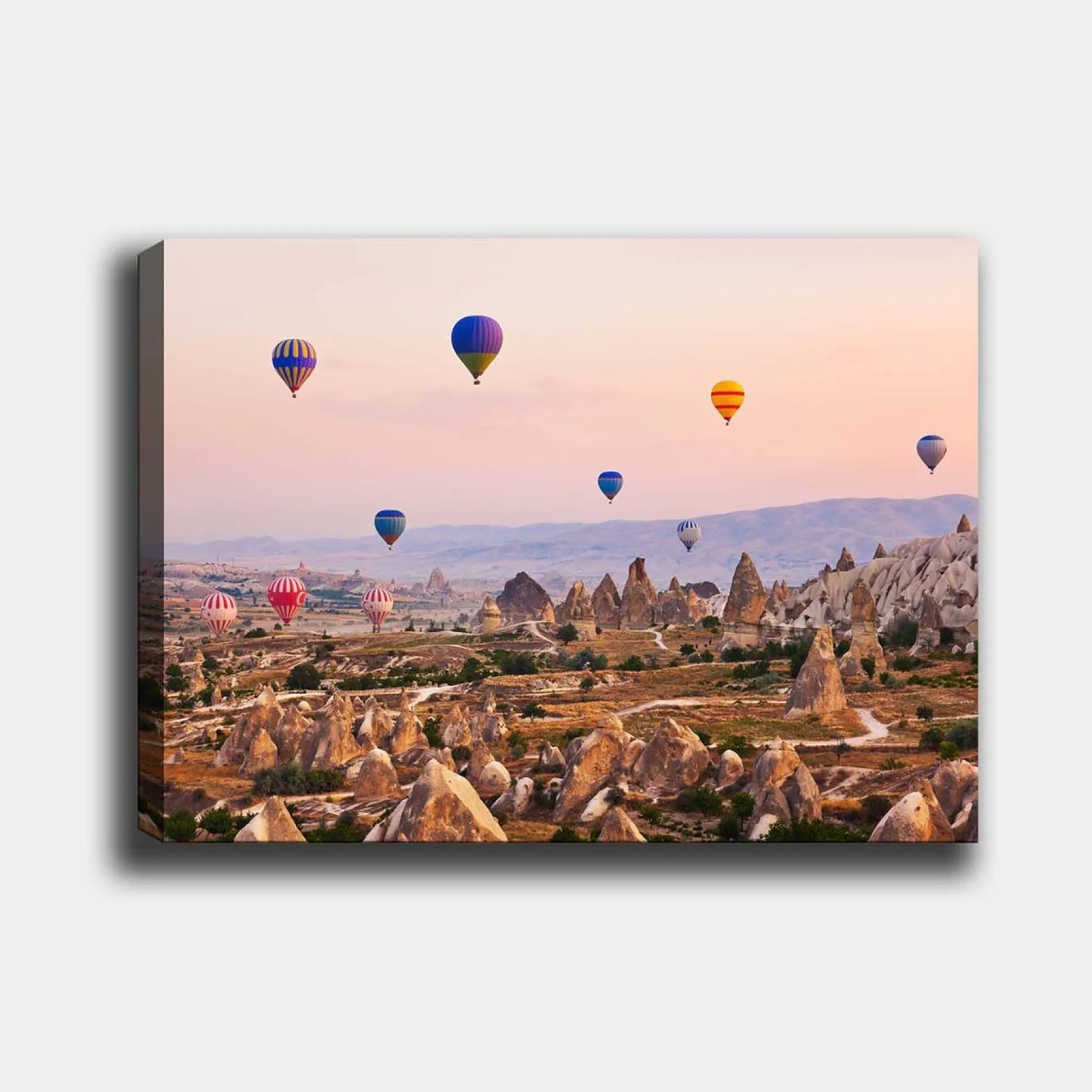 Lerretsbilde 70x100 cm - Flere fargerike varmluftsballonger svever over et dramatisk landskap med unike fjellformasjoner