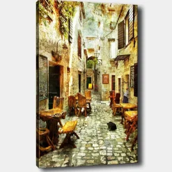 Lerretsbilde 70x100 cm - Pittoresk smug med trebord og stoler, omgitt av gamle steinhus