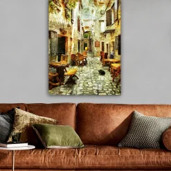 Lerretsbilde 70x100 cm - Pittoresk smug med trebord og stoler, omgitt av gamle steinhus